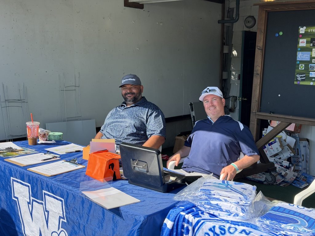 Volunteers seated at the Wilcoxson Fathers Club golf tournament check-in table.
