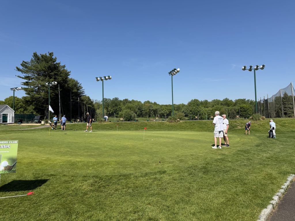 Golfers standing on a putting green during the Wilcoxson Fathers Club Golf Tournament.
